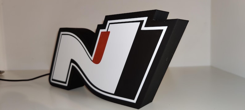 May include: A large, three-dimensional sign featuring the letter "N" in a stylized design. The sign has a black border, a white interior with a red accent, and a white outline. The sign is angled, showcasing its depth and design.