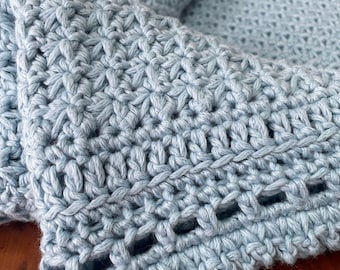 May include: A light blue crocheted blanket with a delicate openwork border. The blanket is made with a soft yarn and has a textured, hand-stitched look.