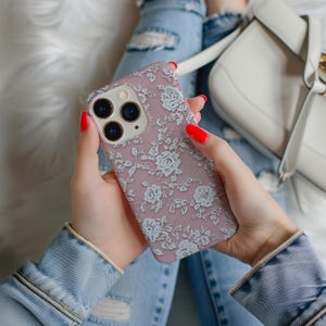 May include: A pink iPhone case with a white floral pattern. The case is made of silicone and has a matte finish.