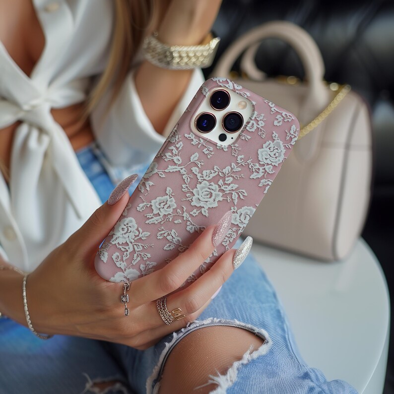 May include: A pink phone case with a white floral pattern. The case has a camera lens cutout and is made of a soft, flexible material.