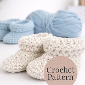 May include: Close-up of cream-coloured crochet baby booties with a folded cuff, alongside a ball of light blue yarn and a pair of blue crochet booties. The image includes the text "Crochet Pattern" on a circular background.