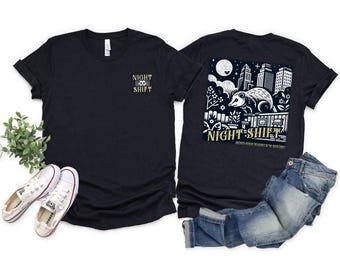 May include: Black t-shirt with the text "NIGHT SHIFT" in gold on the front and a graphic on the back featuring an opossum, city skyline, and the words "NIGHT SHIFT". Includes a pair of white trainers and blue jeans.