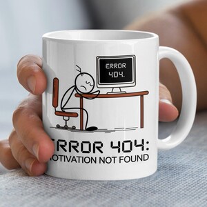 May include: White ceramic mug featuring a stick figure slumped over a desk with a computer screen displaying "ERROR 404." The mug also has the text "ERROR 404: MOTIVATION NOT FOUND" below the stick figure and desk.