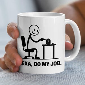 May include: White ceramic mug with a black stick figure design. The illustration depicts a stick figure at a desk with a smart speaker. The text on the mug reads "ALEXA, DO MY JOB."