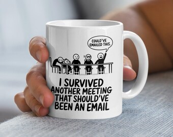 Puede incluir: Taza de cerámica blanca con un gráfico negro de figuras de palo en una mesa, con el texto "I SURVIVED ANOTHER MEETING THAT SHOULD'VE BEEN AN EMAIL." Un bocadillo dice "COULD'VE EMAILED THIS."