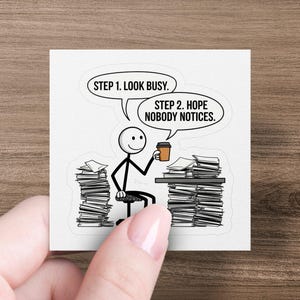 May include: A black and white illustration of a stick figure sitting at a desk with a large stack of papers on either side. The stick figure is holding a cup of coffee and the text above reads "Step 1. Look Busy. Step 2. Hope Nobody Notices."