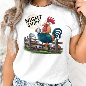 Può includere: Maglietta bianca con una grafica di un gallo che tiene una tazza di caffè e il testo "NIGHT SHIFT". Il gallo è in piedi su una recinzione con altri animali che dormono dietro di lui.