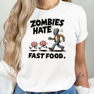 Könnte beinhalten: Weißes T-Shirt mit schwarzem Text, der "Zombies Hate Fast Food" lautet. Die Grafik zeigt einen Zombie, der zwei Gehirne verfolgt.