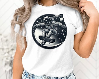 Puede incluir: Camiseta blanca con un gráfico de un astronauta patinando en el espacio. El astronauta lleva un traje espacial y un casco, y la patineta tiene ruedas. El fondo es una ilustración en blanco y negro del espacio con estrellas.