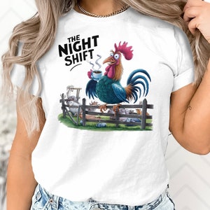 Può includere: Maglietta bianca con una grafica di un gallo che tiene una tazza di caffè e il testo "The Night Shift".