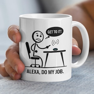 May include: White ceramic mug with a black and white cartoon illustration. The design features a stick figure sitting at a desk, with the text "GET TO IT!" in a speech bubble and the words "ALEXA, DO MY JOB."