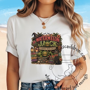 May include: A white t-shirt featuring a graphic of a tropical-themed pumpkin stand with the text WATERMELON JACK, CARVED FRESH DAILY, SWEET, SPOOKY, JUICY, TO DIE FOR, and LOCALLY GROWN. The design includes carved watermelons, a witch hat, and a black cat.