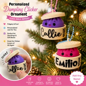 May include: Two personalized dumpling clicker ornaments hanging on a tree, one purple and one pink, each inside a beige bamboo-style steamer basket base with a lid. The base features the name Callie or Emilio and the year 2026 in black text.