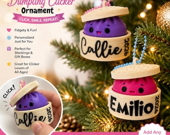 May include: Two personalised dumpling clicker ornaments hanging on a tree, one purple and one pink, each inside a beige bamboo-style steamer basket base with a lid. The base features the name Callie or Emilio and the year 2026 in black text.