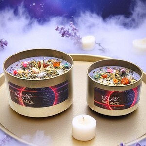 May include: Two gold candle jars with purple wax and embedded crystals. The jars have a black label with the text "Solar Radiance". The candles are on a gold tray with two white tea lights.