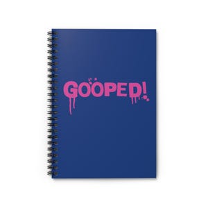Puede incluir: Una libreta espiral azul con la palabra "GOOPED!" escrita en letras rosas con efectos de pintura que gotean.