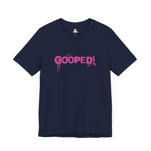 May include: A navy blue t-shirt with a pink graphic that says "GOOPED!" in a dripping paint style.