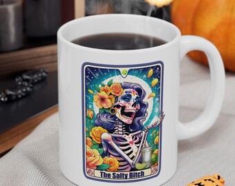 May include: White ceramic coffee mug with a colorful illustration of a skeleton with flowers in her hair and the text "The Salty Bitch".