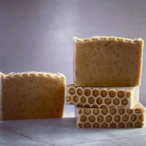 Puede incluir: Cuatro barras de jabón hecho a mano, tres están apiladas una encima de la otra. La barra superior es lisa, la barra del medio tiene un patrón de panal y la barra inferior es lisa. La cuarta barra es lisa y está sentada a la izquierda de la pila.
