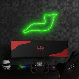 Könnte beinhalten: Ein schwarzer Computermonitor mit einem roten und schwarzen Design und dem Text "MS LAB" auf dem Bildschirm. An der Wand hinter dem Monitor befindet sich ein grünes Neonlicht in Form einer Rennstrecke. Im Vordergrund befindet sich ein schwarzes Rennlenkrad.