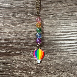 Peut inclure: Un collier en chaîne dorée avec un pendentif en forme de montgolfière arc-en-ciel et des perles de cristal arc-en-ciel.