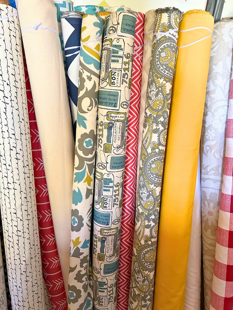 Pu&ograve; includere: Una collezione di rotoli di tessuto con vari motivi e colori. I disegni includono stampe floreali, paisley, chevron e a tema viaggio. I colori vanno dal rosso, bianco e blu al giallo e grigio. Alcuni rotoli hanno il testo "BON VOYAGE 75116".