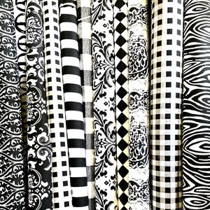 Pu&ograve; includere: Una collezione di rotoli di tessuto con vari motivi in bianco e nero. I disegni includono strisce, quadri, damasco e rombi. I tessuti sono arrotolati strettamente, mostrando le diverse trame e stili.