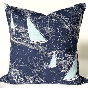 May include: Square navy blue pillow with a nautical map design. The pillow features a detailed white map pattern with light blue sailboats scattered across the surface. The pillow is a decorative item for a nautical or coastal themed home.