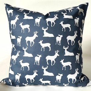 Pu&ograve; includere: Un cuscino quadrato decorativo con sfondo blu navy e un motivo ripetuto di sagome di cervi bianchi. I cervi sono in varie pose. Il cuscino ha un aspetto morbido e strutturato, ideale per l'arredamento della casa.