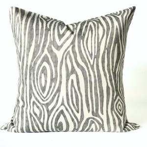 May include: Square decorative pillow with a gray and white wood grain pattern. The pillow has a neutral color palette and a textured appearance, suitable for home decor. The pillow is a square shape.
