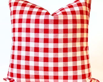 May include: Square pillow with a red and white checkered pattern. The pillow has a classic gingham design, with evenly spaced red and white squares. The pillow is a decorative item, suitable for a living room or bedroom.