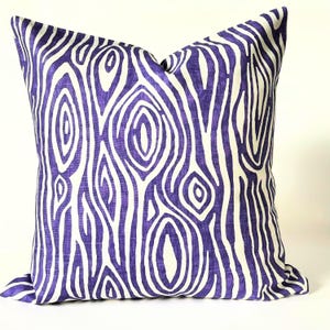 May include: Square decorative pillow with a purple and white abstract pattern. The design features a series of organic, swirling shapes resembling wood grain. The pillow is made of a textured fabric and is suitable for a sofa or bed.