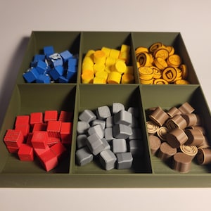 May include: A green wooden box with six compartments, each filled with different coloured game pieces. The compartments contain red, blue, grey, yellow, brown, and gold pieces.