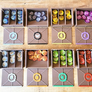 Puede incluir: Un conjunto de 10 cajas de almacenamiento de madera con tapas, cada una con un símbolo y un color diferente. Las cajas están divididas en compartimentos y contienen pequeñas fichas o piezas de juego.