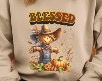 May include: Beige sweatshirt with the word "BLESSED" in a fall-themed font. The graphic features a smiling scarecrow with a pumpkin head, wearing a hat and overalls, with a pumpkin and fall foliage.
