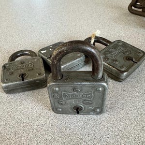 May include: Four vintage metal padlocks with the word "Master" printed on them. The padlocks are silver and gray with a worn, aged look.