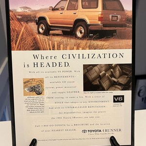 Peut inclure: Publicité encadrée pour le Toyota 4Runner 1995. L'image présente un SUV doré sur un chemin sablonneux, avec le texte « Where Civilization is Headed ». Comprend des détails sur le moteur V6 et les garnitures en cuir.