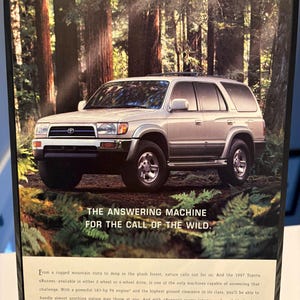 Könnte beinhalten: Werbung für den Toyota 4Runner SUV von 1997. Das silberne Fahrzeug wird in einer Waldlandschaft gezeigt. Der Text lautet: „DIE ANTWORTMASCHINE FÜR DEN RUF DER WILDNIS“. Das Toyota-Logo ist sichtbar.