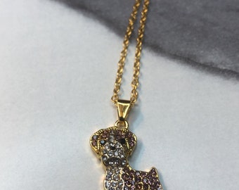 Può includere: Collana dorata con un ciondolo a forma di cane. Il ciondolo è impreziosito da cristalli trasparenti e viola, creando un effetto scintillante. Il design del cane è dettagliato, con la catena che aggiunge un tocco delicato. Un accessorio elegante per gli amanti degli animali.