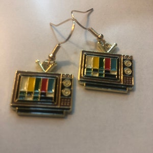 Op de afbeelding: Een paar gouden oorbellen met een vintage televisieontwerp met een kleurrijk testpatroon op het scherm. De oorbellen hebben een haaksluiting.