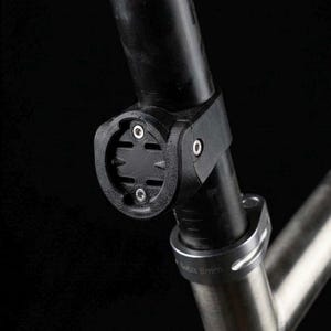 Pode incluir: Um suporte de espigão de selim de bicicleta preto com uma interface de fixação circular e dois pequenos parafusos prateados. O suporte está fixado a um poste cilíndrico preto, ligado a um componente de estrutura prateado com o texto 8mm.