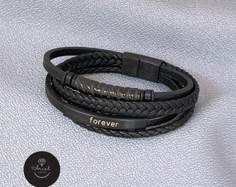 May include: Black leather bracelet with multiple strands, featuring a braided design and a metal bar engraved with the word "forever." The bracelet has a magnetic clasp and a dark, matte finish. The Ariel Jewelry logo is in the lower left corner.