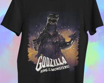 Könnte beinhalten: Schwarzes T-Shirt mit einem Vintage-Grafik von Godzilla, dem König der Monster. Das Design enthält den Text "GODZILLA OF KING THE MONSTERS!" in Weiß. Das T-Shirt hat kurze Ärmel und einen Rundhalsausschnitt. Ein Klassiker.