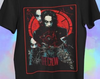 May include: Black t-shirt featuring a graphic from "The Crow" movie. The design includes a central figure with white face paint, surrounded by a red clock-like background and the text "THE CROW" in red. The shirt is a classic crew neck.