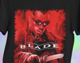 May include: Black t-shirt with a red graphic of a man in sunglasses, holding a sword. The word "BLADE" is printed in white. The graphic has a red, textured background, creating a striking contrast against the black fabric.