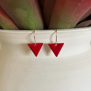 May include: A pair of red triangle earrings with gold hoops. The earrings are small and delicate.