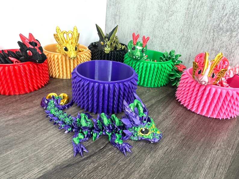 May include: A selection of vibrant 3D-printed dragon ornaments and coordinating decorative pots. The dragons are in shades of purple, green, gold, red, and pink. The pots are cylindrical with textured sides.