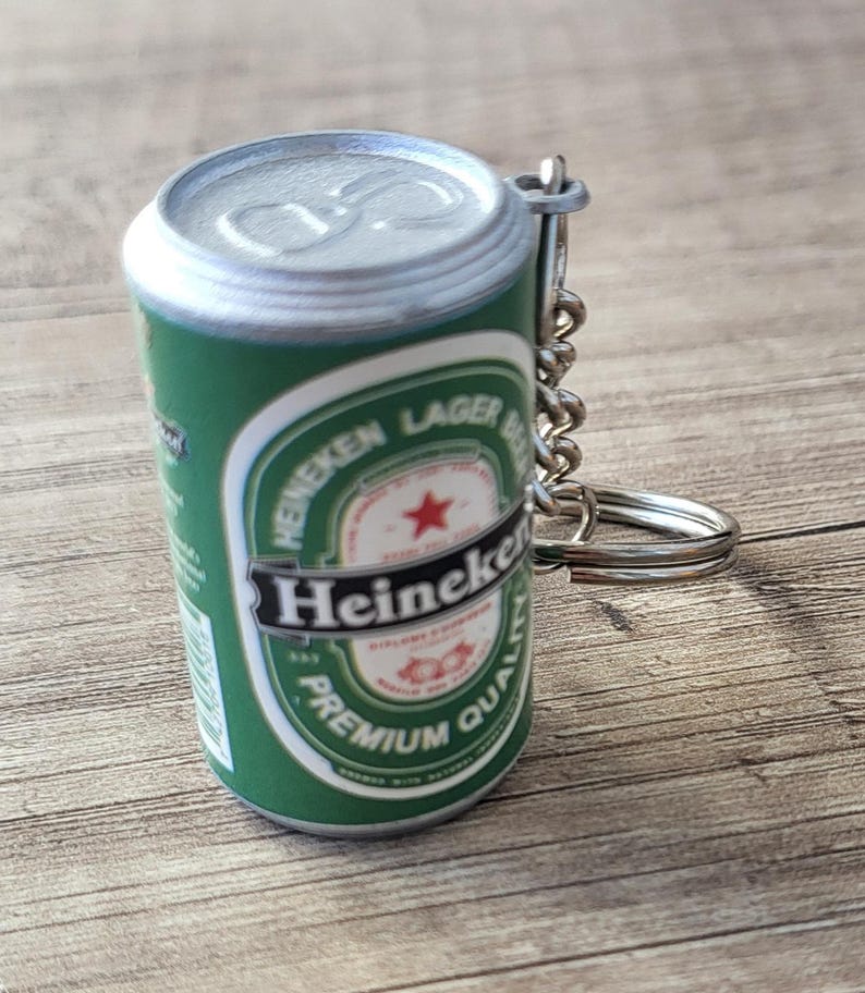 May include: Miniature green and silver Heineken Lager Beer can keychain. The can features the Heineken logo, a red star, and the words "PREMIUM QUALITY". A silver chain and keyring are attached.