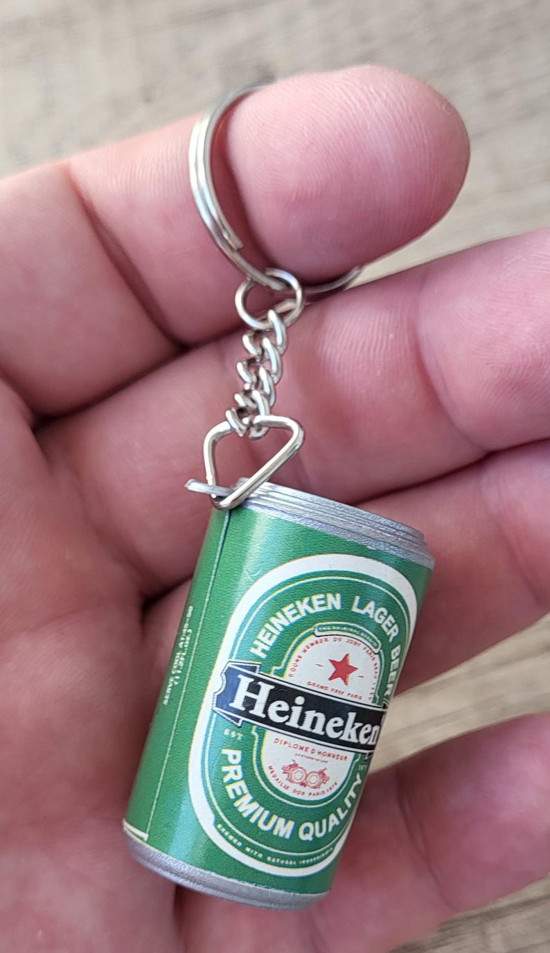 May include: Miniature Heineken Lager Beer can keychain. The green and white can features the Heineken logo and text. The keychain has a silver-colored ring and chain.