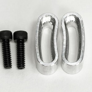 May include: Two black hex head bolts and two silver-colored, curved metal pieces are displayed against a white background. The bolts have a threaded shaft and a circular head. The metal pieces have an oval shape with a hollow center.